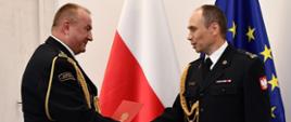 Pomorski Komendant Wojewódzki PSP st. bryg. Jacek Niewęgłowski podczas wręczania aktu powołania Zastępcy Komendanta Powiatowego Państwowej Straży Pożarnej w Człuchowie bryg. Marcinowi Owczarskiemu. W tle flaga państwowa i flaga unii europejskiej.