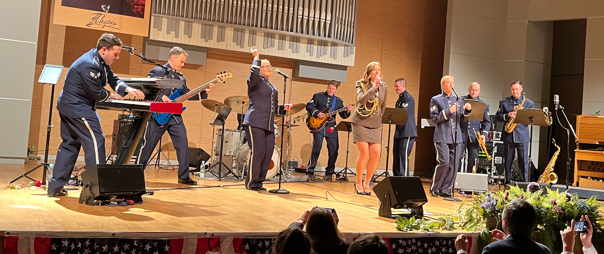 Zdjęcie z koncertu „Ambassadors Rock Band”, który zagrał w Sali Koncertowej ZPSM im. F. Chopina w Jarosławiu. Po lewej stronie muzyk grający na dwóch instrumentach klawiszowych firmy Nord Stage, obok gitarzysta basy grający na gitarze basowej firmy Sadowsky koloru niebieskiego obok niego perkusista, obok perkusji gitarzysta elektryczny obok sekcja instrumentów dętych - puzonista, trębacz i saksofonista. Przed nimi centralnie na scenie trzy wokalistki - na środku st. szer. Anna Khabarova z Reprezentacyjnej Orkiestry Sil Zbrojnych Ukrainy, po jej stronie lewej i prawiej wokalistki USAFE BAND
18 października 2022 r. - fot. Piotr Polański