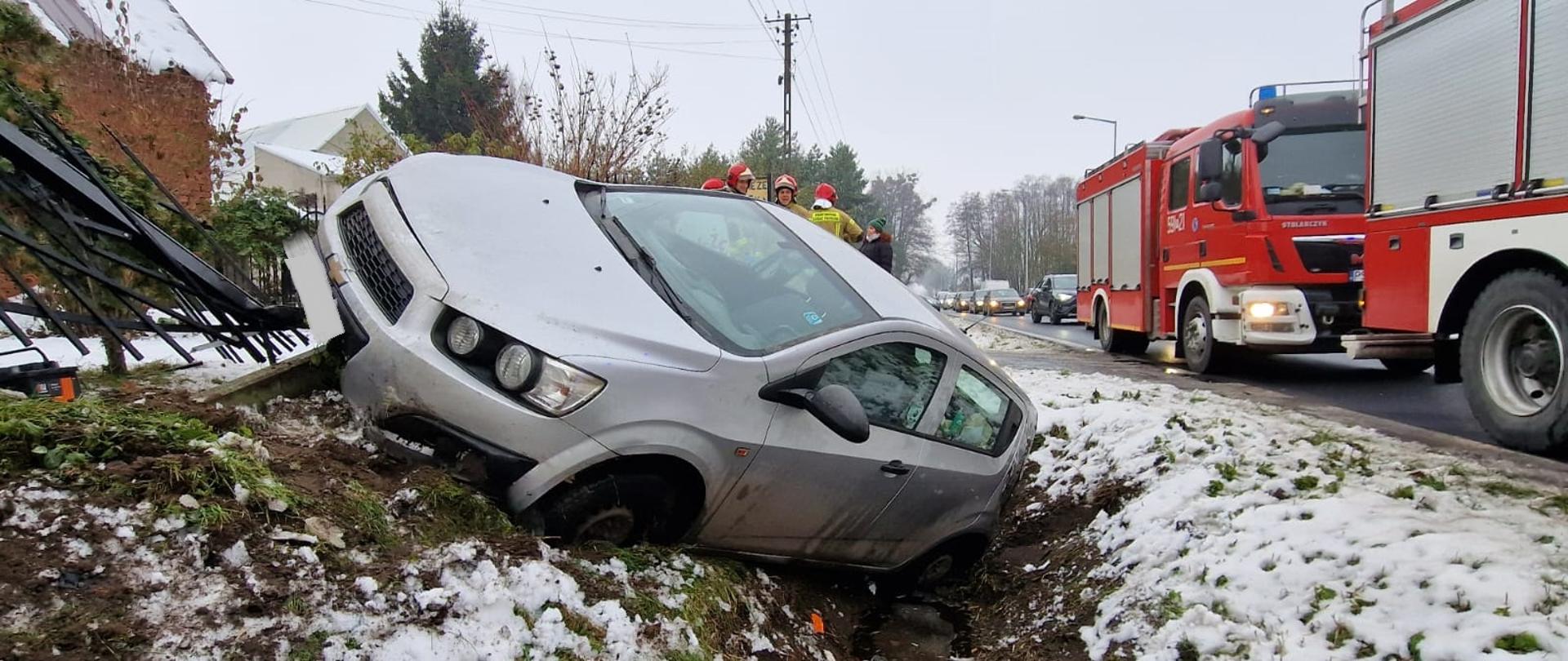 Samochód w rowie, po lewej uszkodzony płot, po prawej samochody strażackie