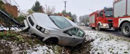 Samochód w rowie, po lewej uszkodzony płot, po prawej samochody strażackie