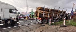 Ciężarówka przewożąca bale drewniane zjechała z drogi i przewróciła się na pobocze. Za nią stoi TiR który sie z nia zderzył.