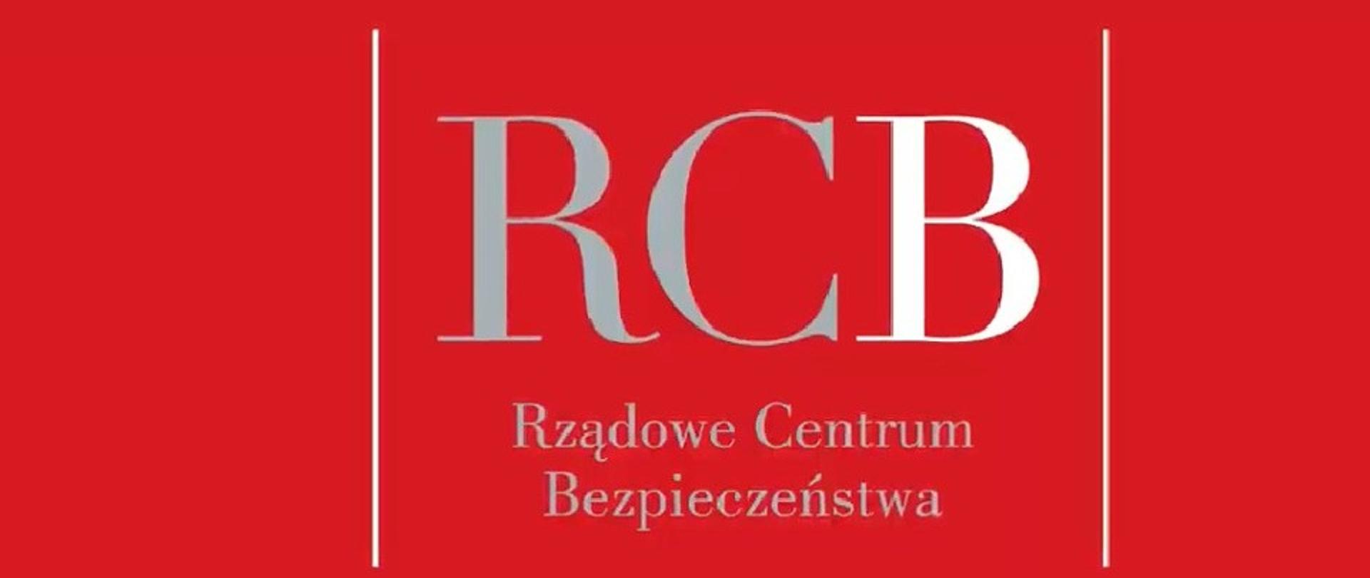Zdjęcie przedstawia logo Rządowego Centrum Bezpieczeństwa. Logo ma czerwone tło na którym umieszczono duży napis w kolorze biało szarym o treści RCB rządowe centrum bezpieczeństwa. Na dole logo podane są adresy strony internetowej oraz portalów społecznych rządowego centrum bezpieczeństwa. 