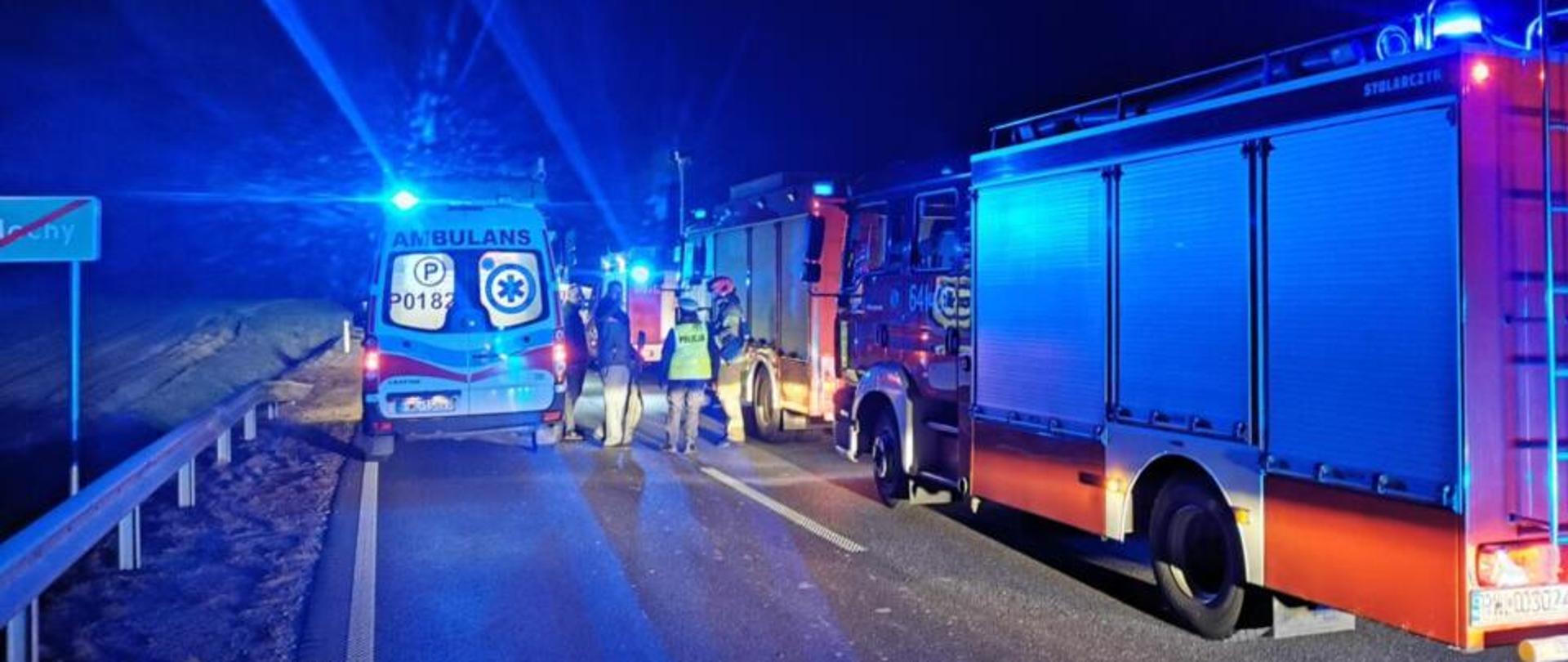 Noc, po prawej samochody strażackie, po lewej karetka.