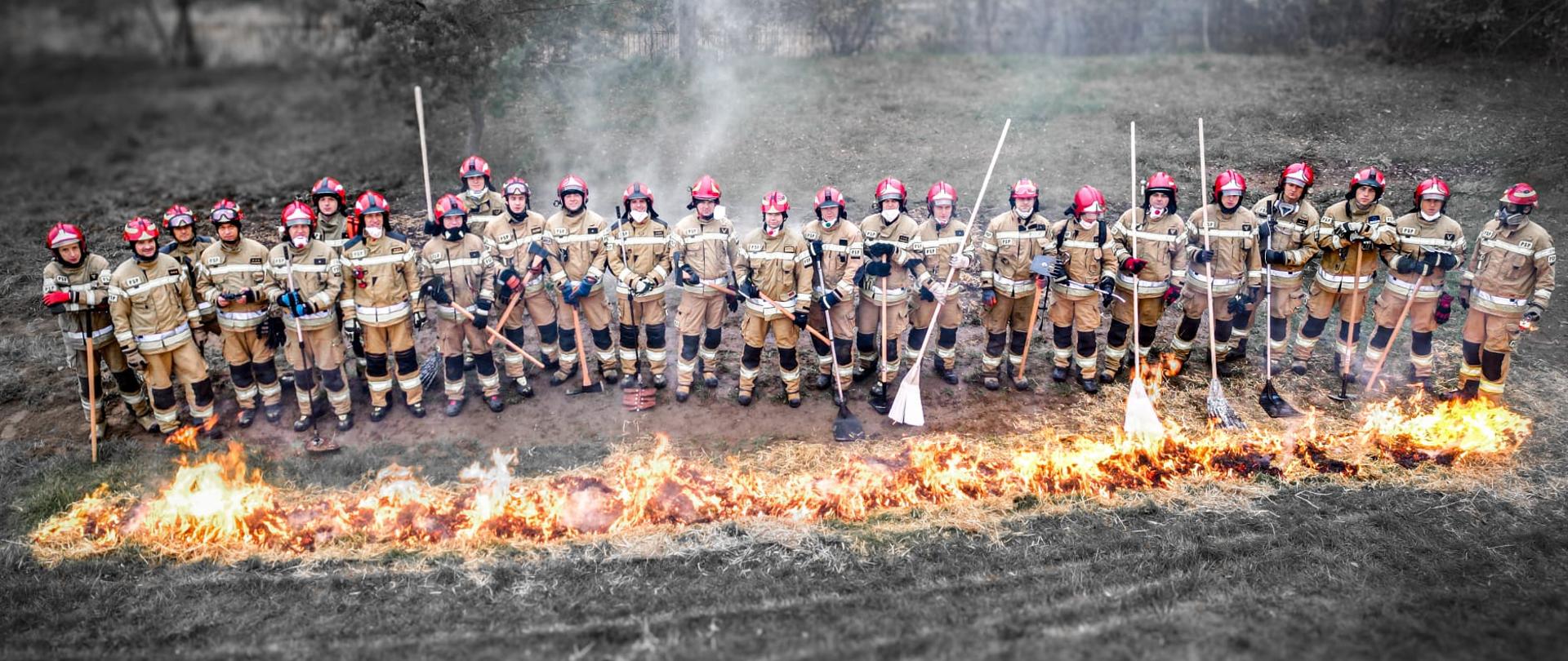 Zdjęcie grupowe z drona, uczestnicy stoją w linii, przed nimi pożar.