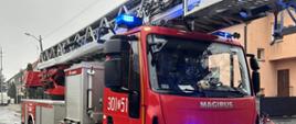 Na pierwszym planie samochód pożarniczy z drabiną mechaniczną na ulicy.