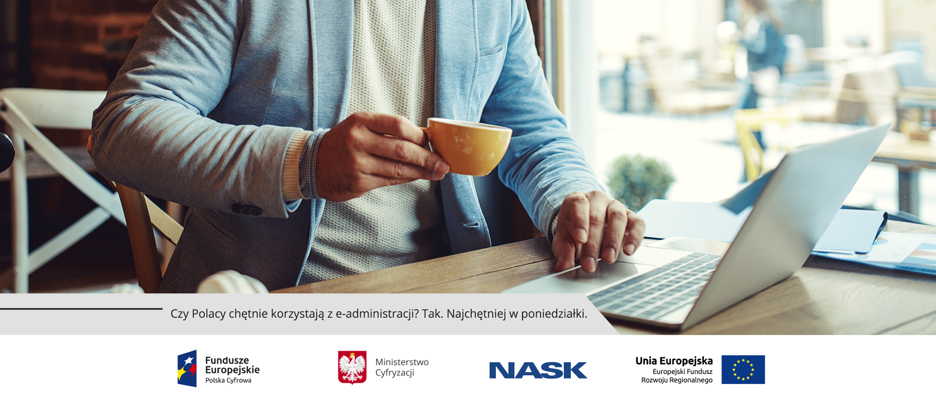 Mężczyzna w marynarce siedzący przy laptopie i popijający napój z filiżanki.