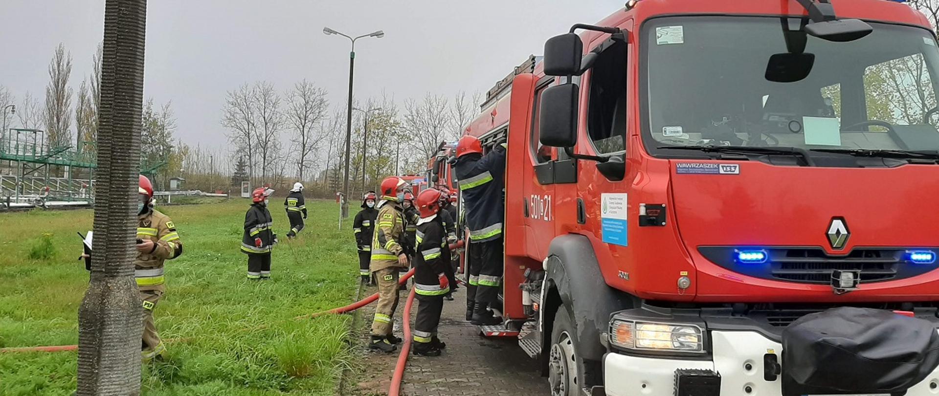 Samochód gaśniczy oraz stojący obok strażacy