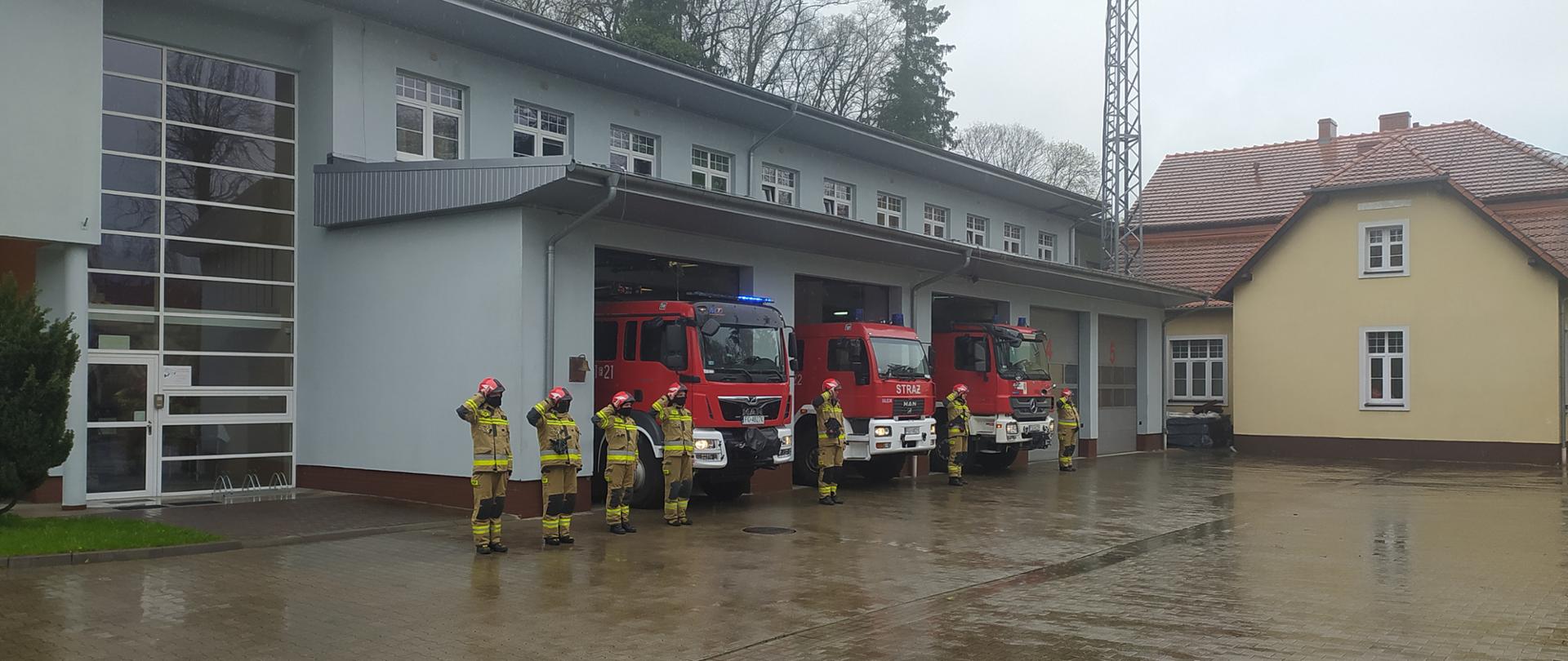 Strażacy przed budynkiem JRG, w tle pojazdy.