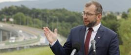 Minister funduszy i polityki regionalnej Grzegorz Puda stoi przed dwoma mikrofonami i przemawia