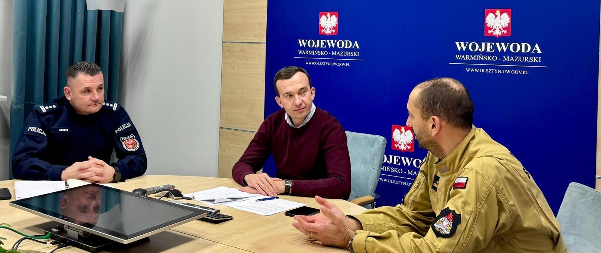 3 mężczyzn rozmawia przy stole konferencyjnym, 2 z nich ma mundur 