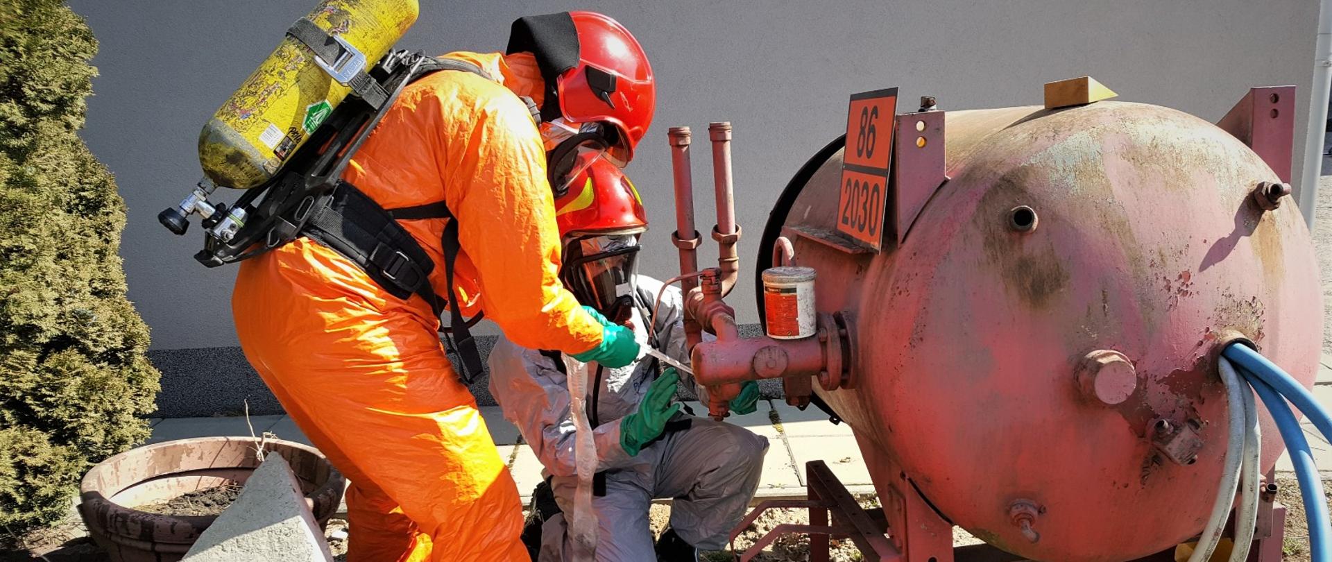 Dwóch strażaków próbuje uszczelnić wyciek 