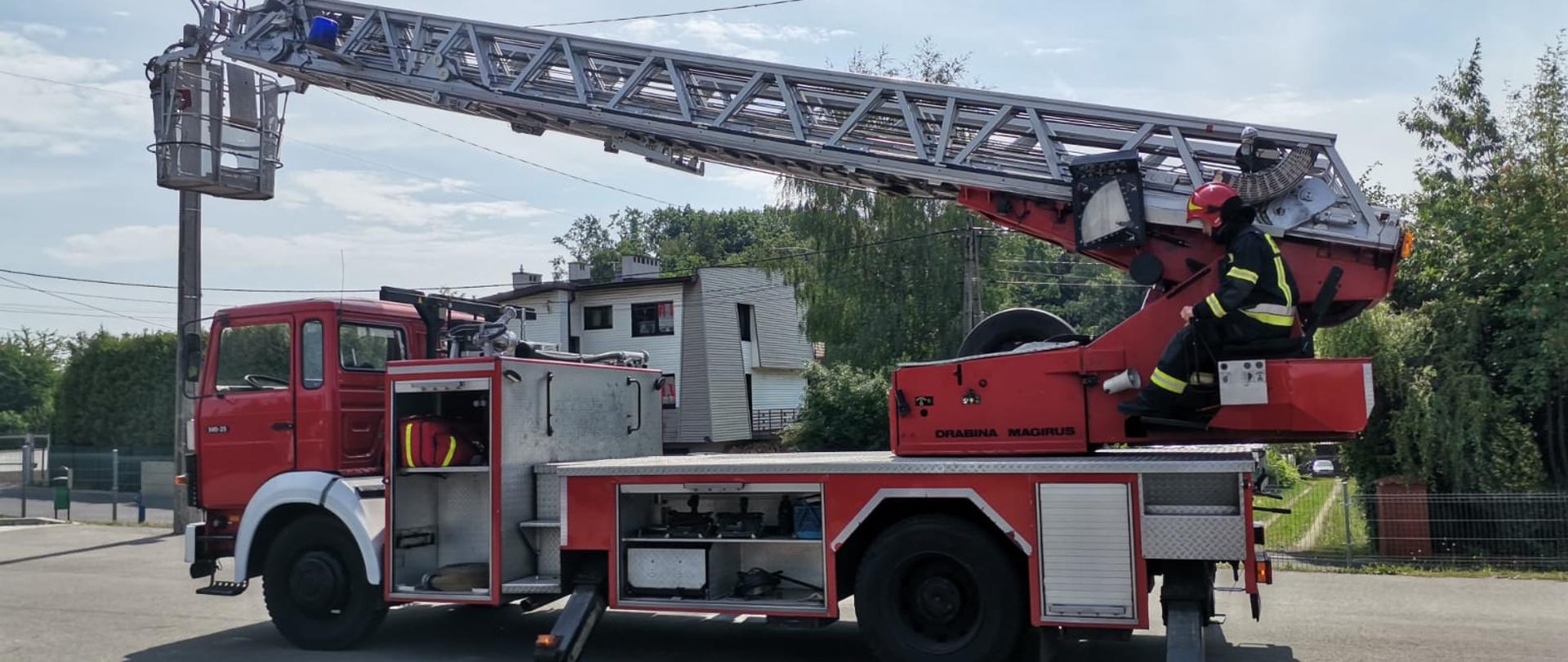 Na samochodzie specjalnym, na fotelu operatora drabiny siedzi strażak 