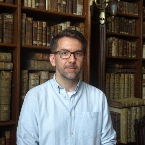 Postać mężczyzny, w tle na półkach zabytkowe księgozbiory.