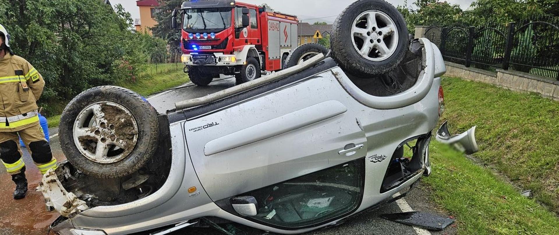 Samochód osobowy na dachu na środku drogi w tle samochód pożarniczy.