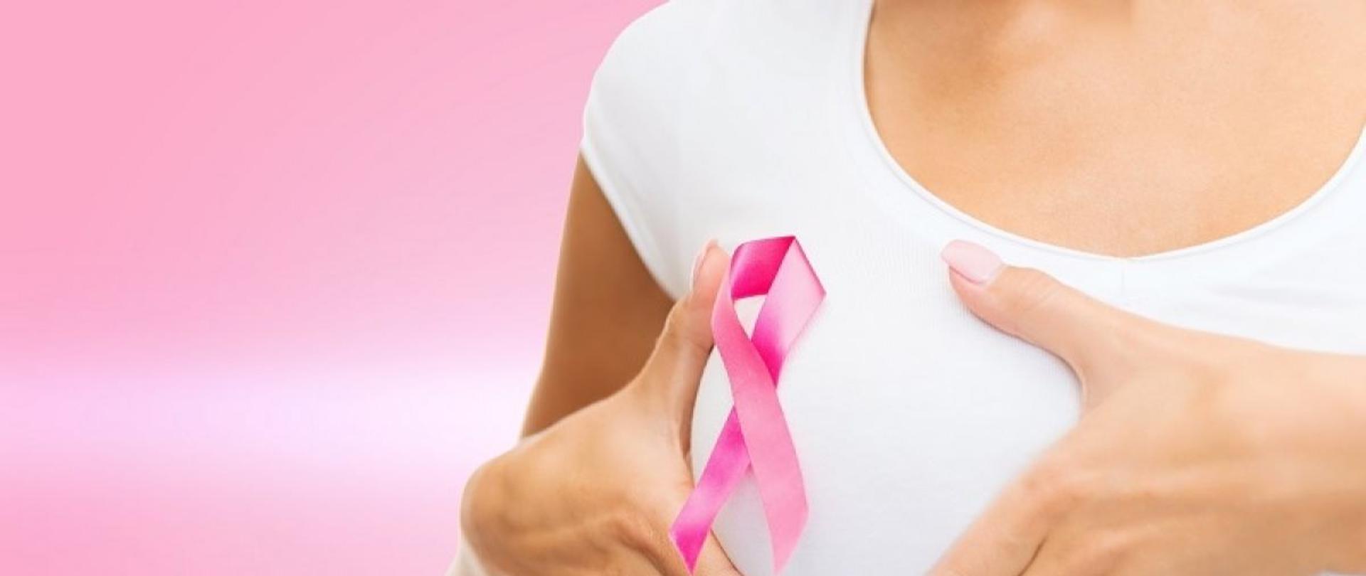 Na różowym tle od prawej strony widoczne ręce kobiety obejmujące prawą pierś kobiety. Kobieta ma na sobie białą koszulkę na której widnieje różowa wstążeczka.