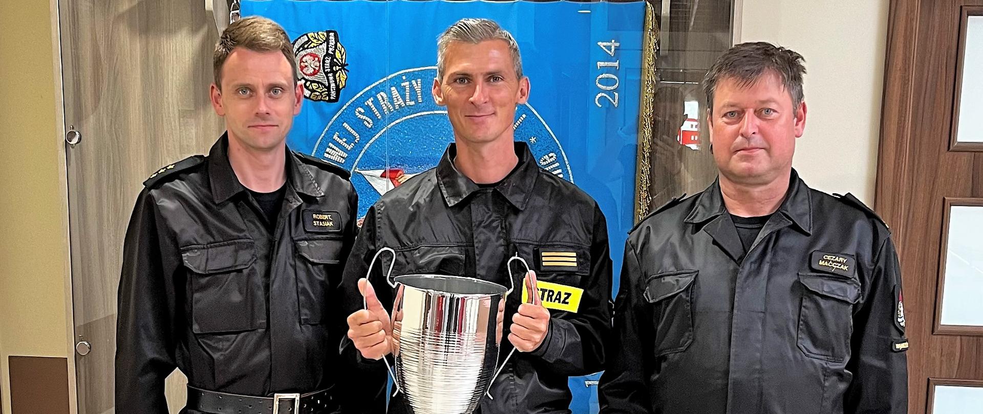 Komendanci powiatowi PSP w Wąbrzeźnie oraz st.sekc. Marian Łazarski trzymający puchar drużynowego Mistrza Polski Komendanta Głównego.