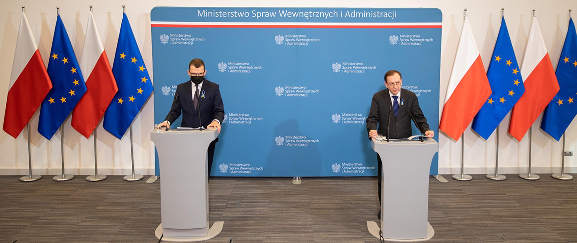 Minister Mariusz Kamiński oraz Paweł Szefenaker stojący przy mównicach podczas konferencji prasowej w MSWiA.