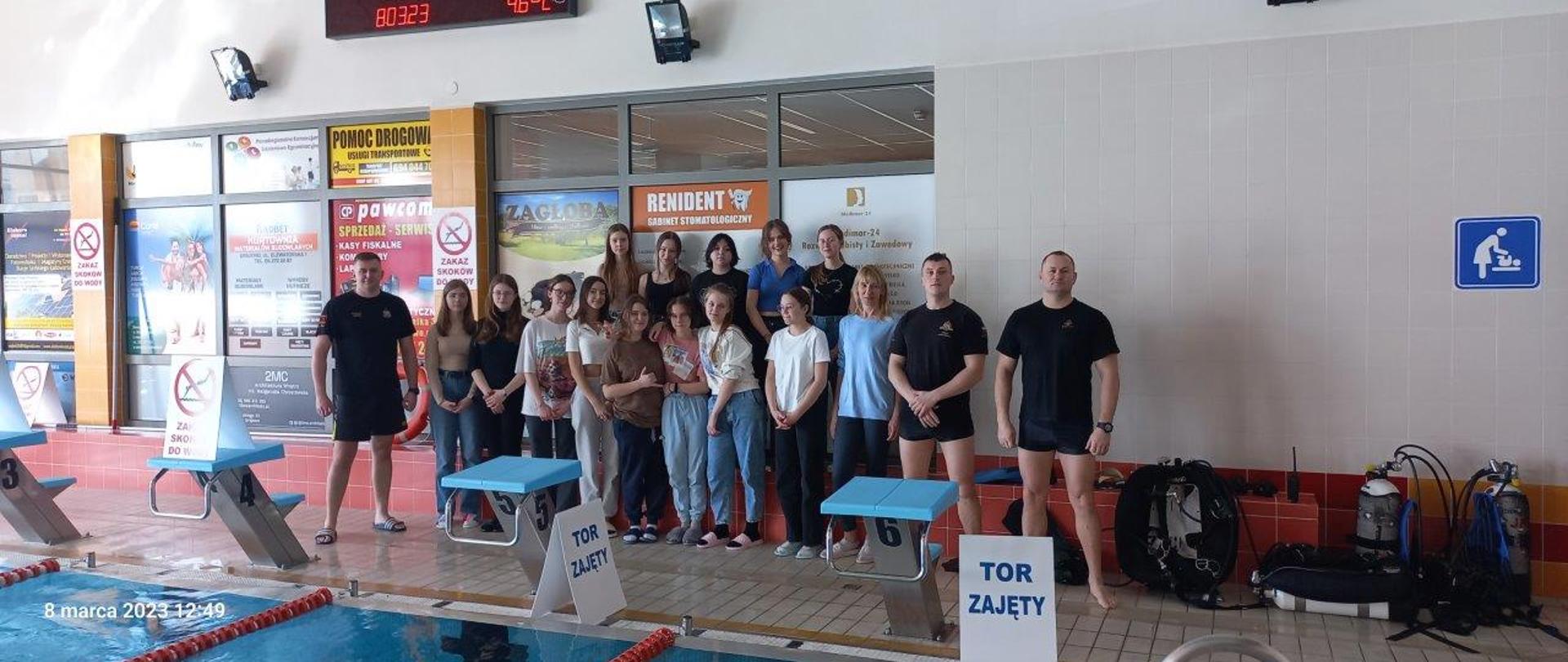 Zdjęcie grupowe. Strażacy oraz uczestnicy zajęć nad niecką basenu.