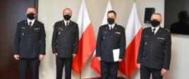 Na zdjęciu widać trzech strażaków w umundurowaniu wyjściowym. W tle trzy flagi Polski.