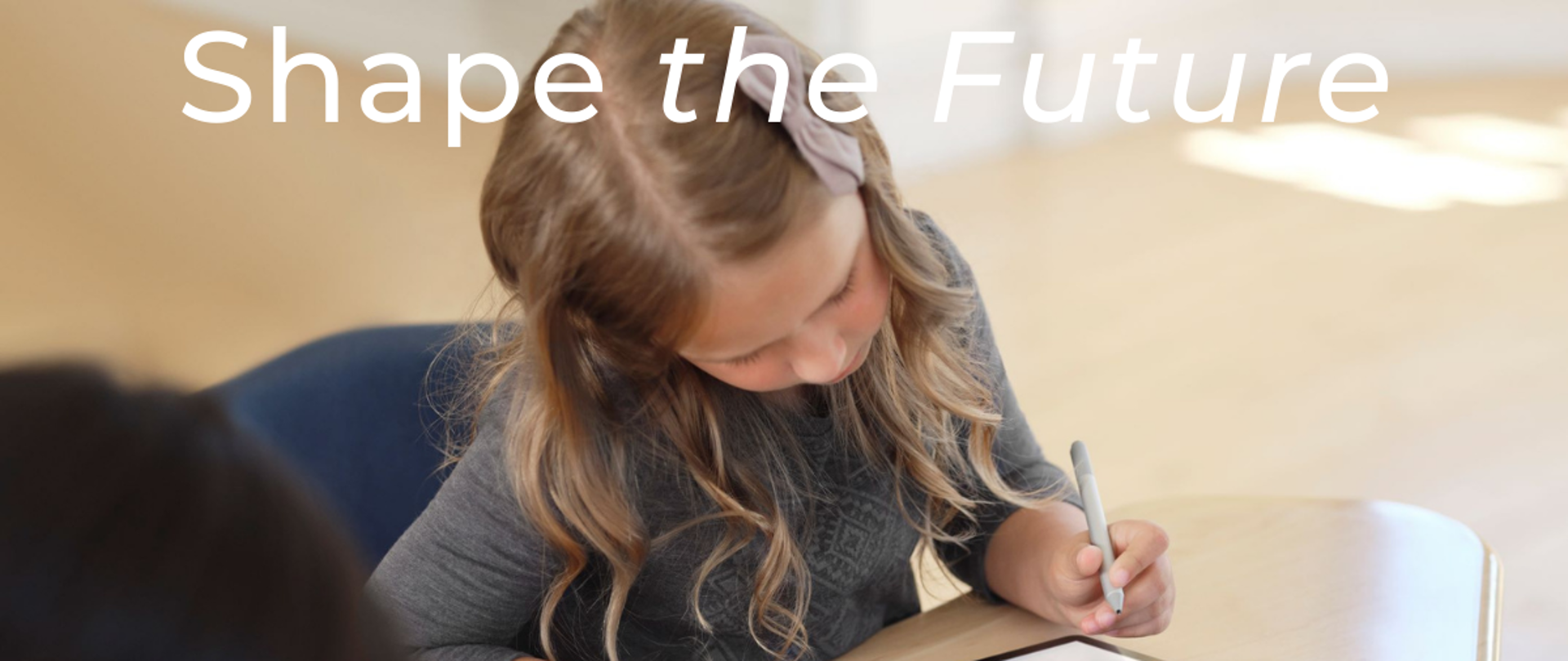 Dziewczyna siedzi przy biurku w ławce, w ręku ma tablet i mazak. Obok jakiś chłopiec. Widać tylko kawałek jego głowy. Dziewczynka ma długie blond włosy i kokardę we włosach. Jej głowa jest przekręcona na bok tak, że dokładnie nie widać jej twarzy. Na dole i na górze napis Shape the future razem dla cyfryzacji edukacji. Poniżej na białym pasku logotypy Ministerstwa Edukacji i Nauki, Gov Tech Polska i Microsoft. 