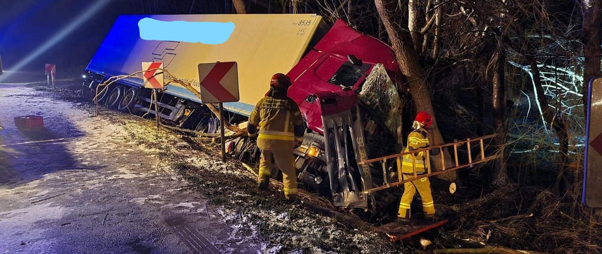 samochód ciężarowy wraz z naczepą w rowie do pojazdu podchodzą strażacy 