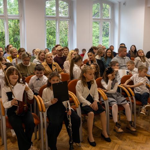 Uczniowie i rodzice zebrani na koncercie uczniów klas pierwszych jako publiczność. Pierwszy rząd zajmują uczniowie występujący na koncercie.
