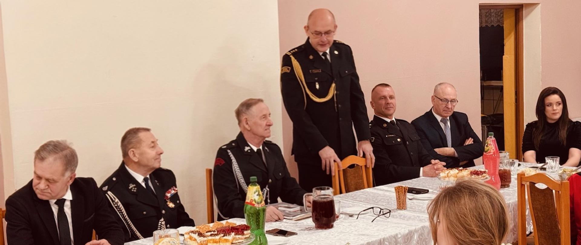 Strażacy i zaproszeni goście siedzą przy stole prezydialnym. Przemawia Z-ca Kujawsko-Pomorskiego Komendanta Wojewódzkiego st. bryg. Artur Przybylski
