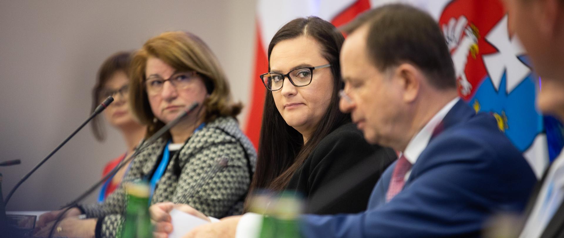 Na zdjęciu cztery osoby siedzące przy mikrofonach. Druga od prawej minister M. Jarosińska-Jedynak.