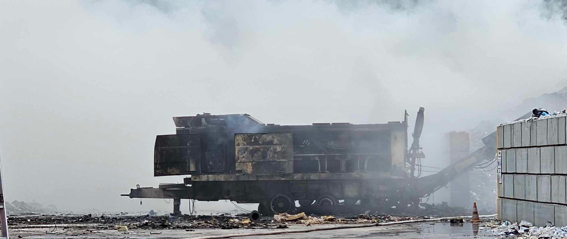 Widzimy podpaloną pryzmę odpadów, nad którą unosi się dym, a przed nią są widoczne pompy wody.