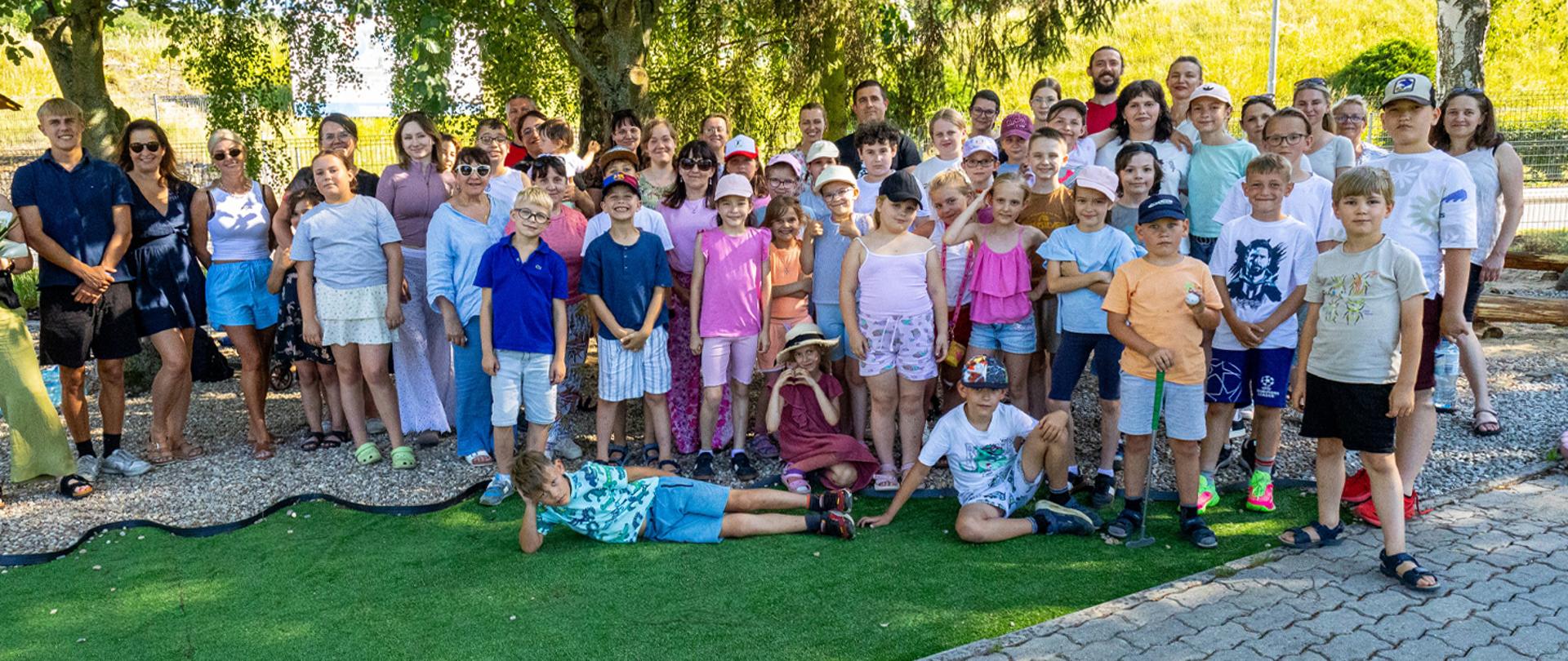 Na zdjęciu grupa kilkudziesięciu osób stojących na polu golfowym.