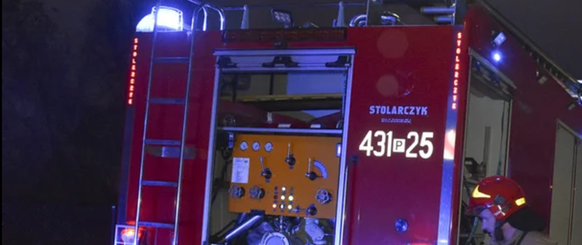 Zdjęcie przedstawia strażaka idącego przy samochodzie pożarniczym.