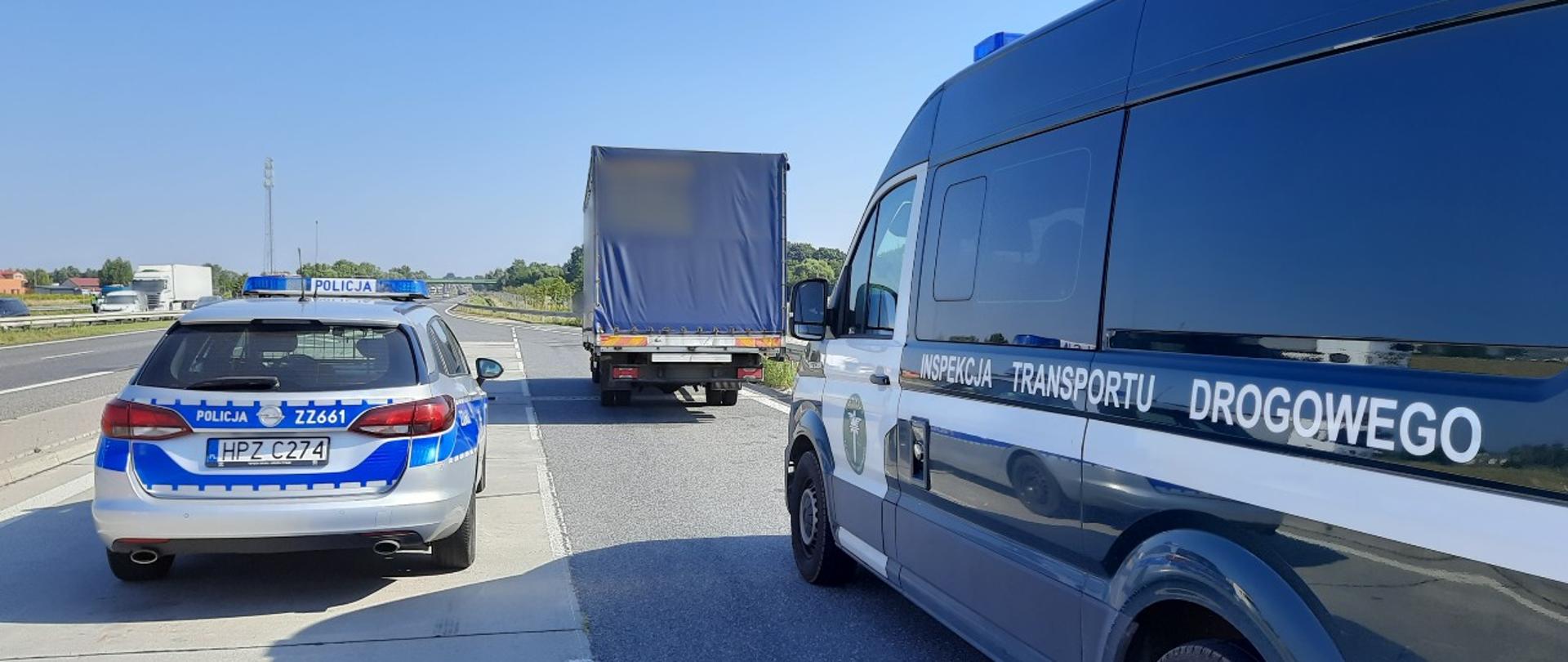 Na pierwszym planie (od lewej): tył oznakowanego radiowozu Policji i lewy bok oznakowanego furgonu Inspekcji Transportu Drogowego. W tle: zatrzymany do kontroli samochód dostawczy. 
