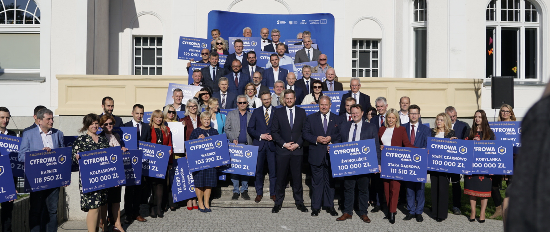 Minister Janusz Cieszyński w Stargardzie wśród samorządowców trzymających symboliczne czeki z kwotami wsparcia, które mogą otrzymać z programu Cyfrowa Gmina.