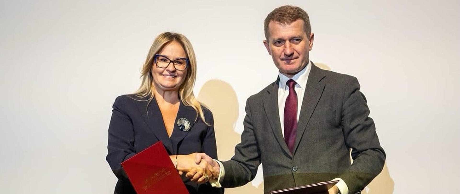 Wicemarszałek województwa kujawsko-pomorskiego i sekretarz stanu w Ministerstwie Sportu i Turystyki Ireneusz Raś podają sobie ręce po podpisaniu porozumienia. Oboje trzymają w rękach teczki.