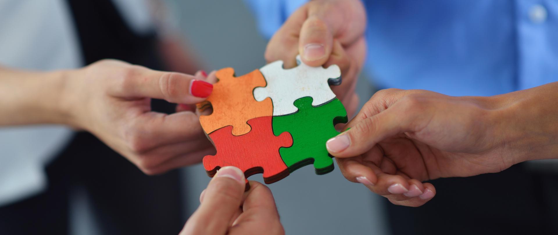 Cztery kolorowe elementy połączone w jeden trzymane przez cztery osoby