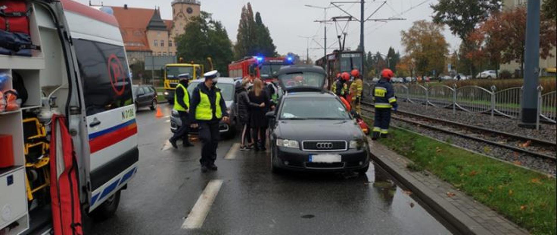 Miejsce w którym doszło wypadku. Widoczna są wozy straży pożarnej, karetka pogotowia oraz uszkodzone pojazdy osobowe. pomiędzy pojazdami widać postaci strażaków, policjantów oraz uczestników zdarzenia.