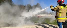 Zdjęcie przedstawia uczestnika kursu podczas zajęć praktycznych, który gasi pożar przy użyciu gaśnicy proszkowej. Na potrzeby szkolenia ogień rozpalono w specjalnej wannie. Zadaniem kursanta było w sposób prawidłowy zgaszenie ognia przy użyciu gaśnicy.