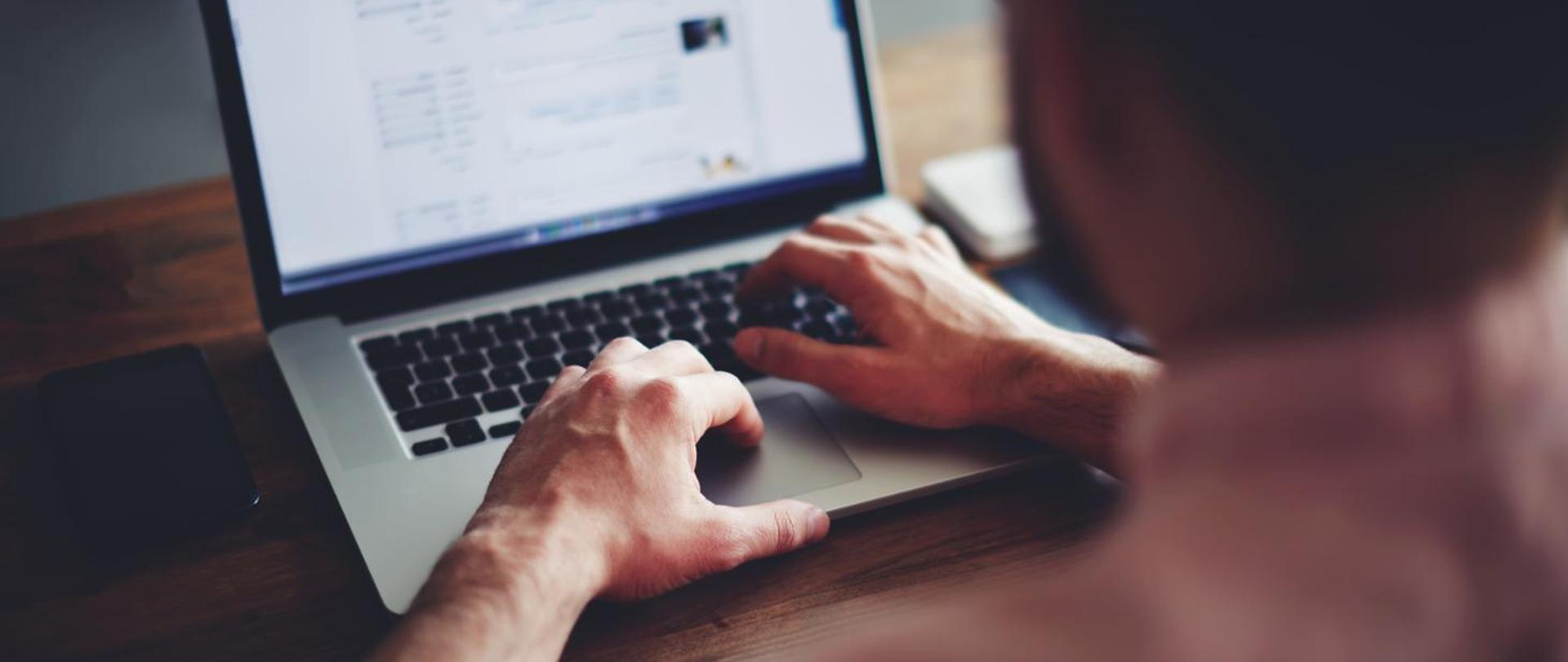 Zdjęcie przedstawiające mężczyznę wykonującego pracę na laptopie