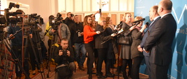 Minister Zdrowia Konstanty Radziwiłł odpowiada na pytania dziennikarzy podczas konferencji prasowej w Łodzi. Minister stoi na tle niebieskiej ścianki z logotypem Ministerstwa Zdrowia, a przed nim ustawieni są dziennikarze z mikrofonami oraz kamery.