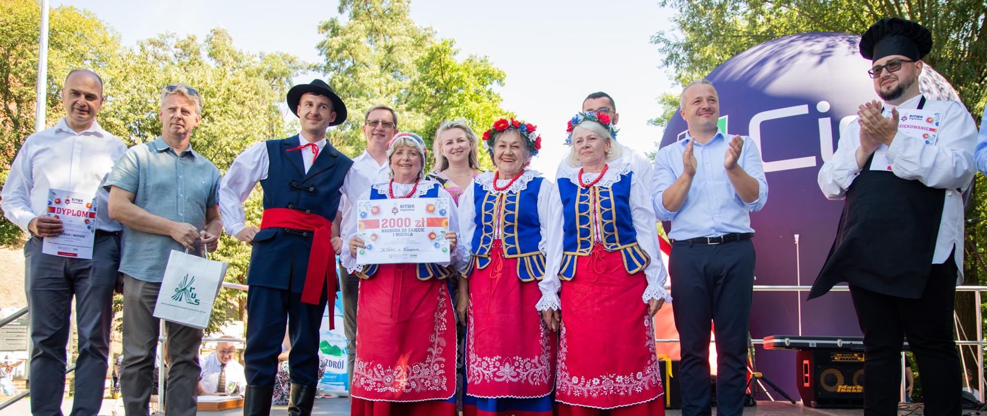 
Grupa ludzi stojąca na scenie w tradycyjnych polskich strojach ludowych
