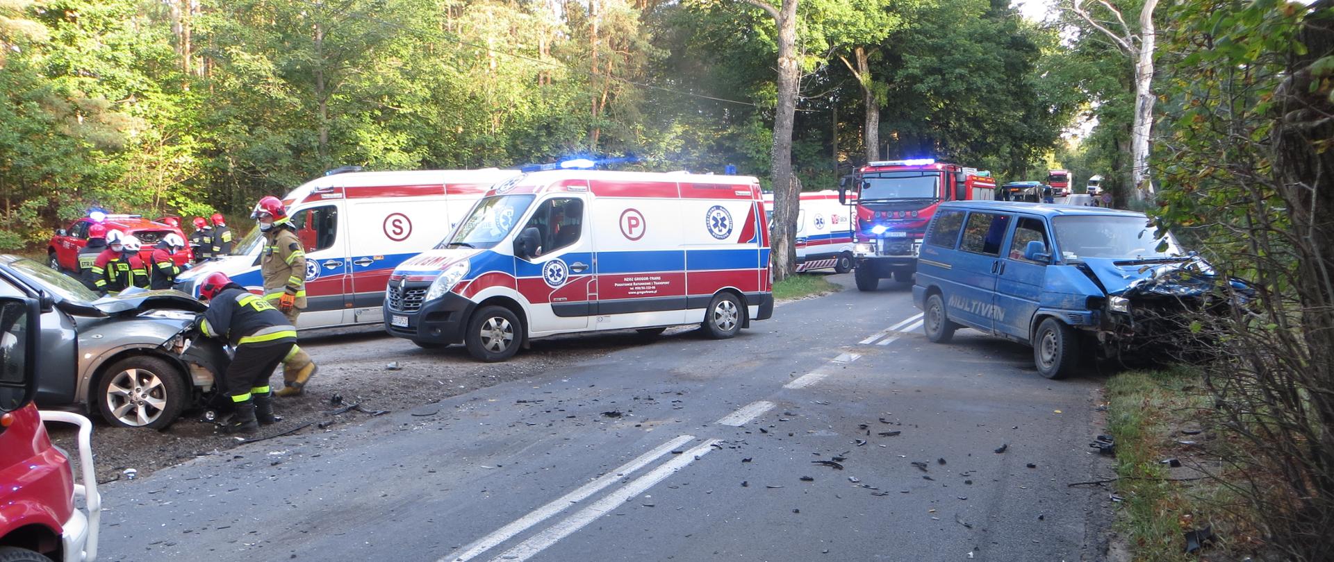 zdjęcie przedstawia miejsce zdarzenia, widać służby ratownicze, pojazdy uczestniczące w kolizji, uszkodzone samochody po kolizji na drodze