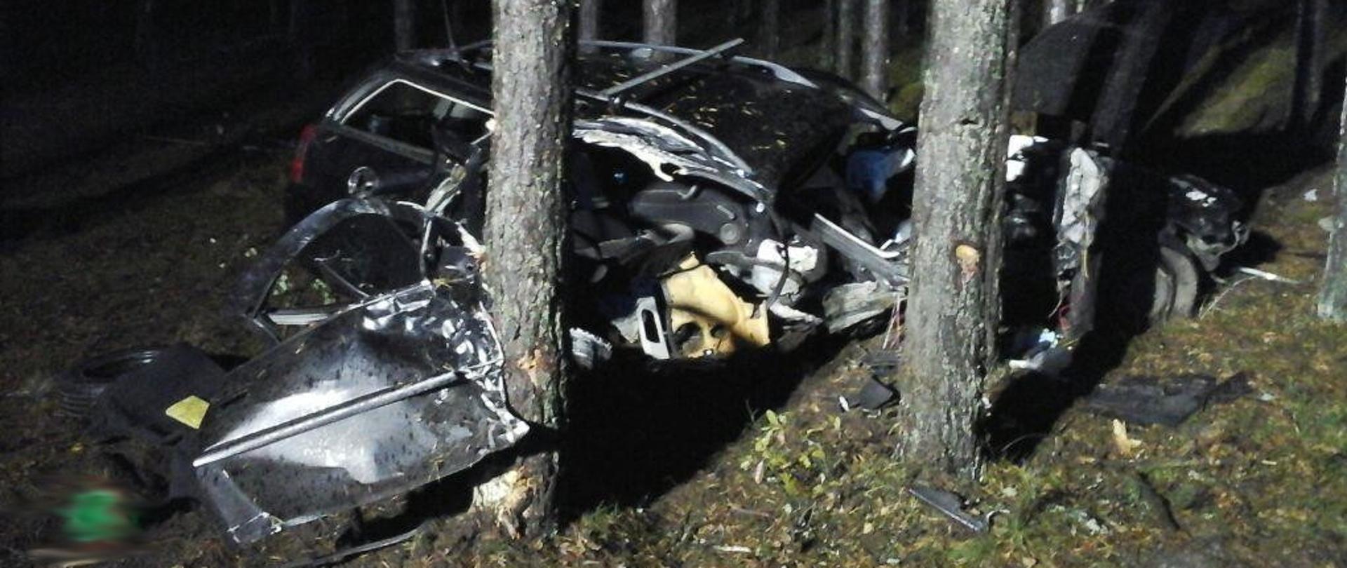 Noc. Rozbity czarny samochód w lesie. Wokół porozrzucane rzeczy, które znajdowały się w aucie. 