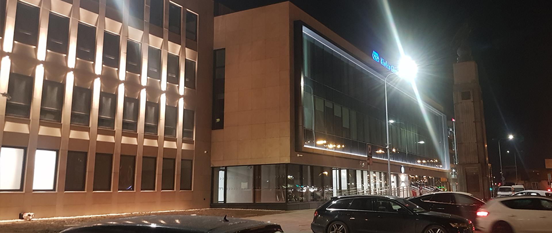 Zabytkowy dworzec PKP w Kielcach po modernizacji, oświetlony nocą, z widocznym logiem KGHM i samochodami na ulicy.