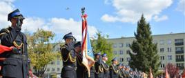 Na zdjęciu widać pododdział strażaków ustawiony w linii podczas uroczystych obchodów dnia strażaka. Na pierwszym planie widoczny jest sztandar Komendy Powiatowej w Olecku.