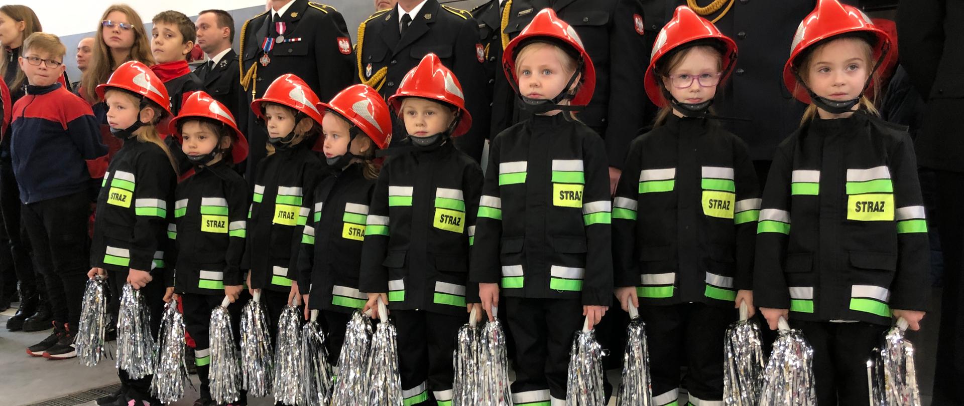 Przed szykiem strażaków KP PSP Krapkowice ustawione przedszkolaki z Przedszkolnej Drużyny Pożarniczej z PP nr 3 w Gogolinie. Dzieci ubrane w mundurki strażackie i czerwone hełmy młodzieżowe. 