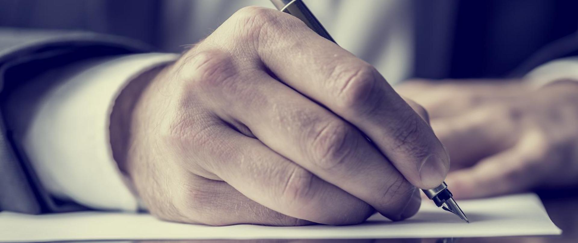 Dłoń trzymająca pióra i pisząca na papierze