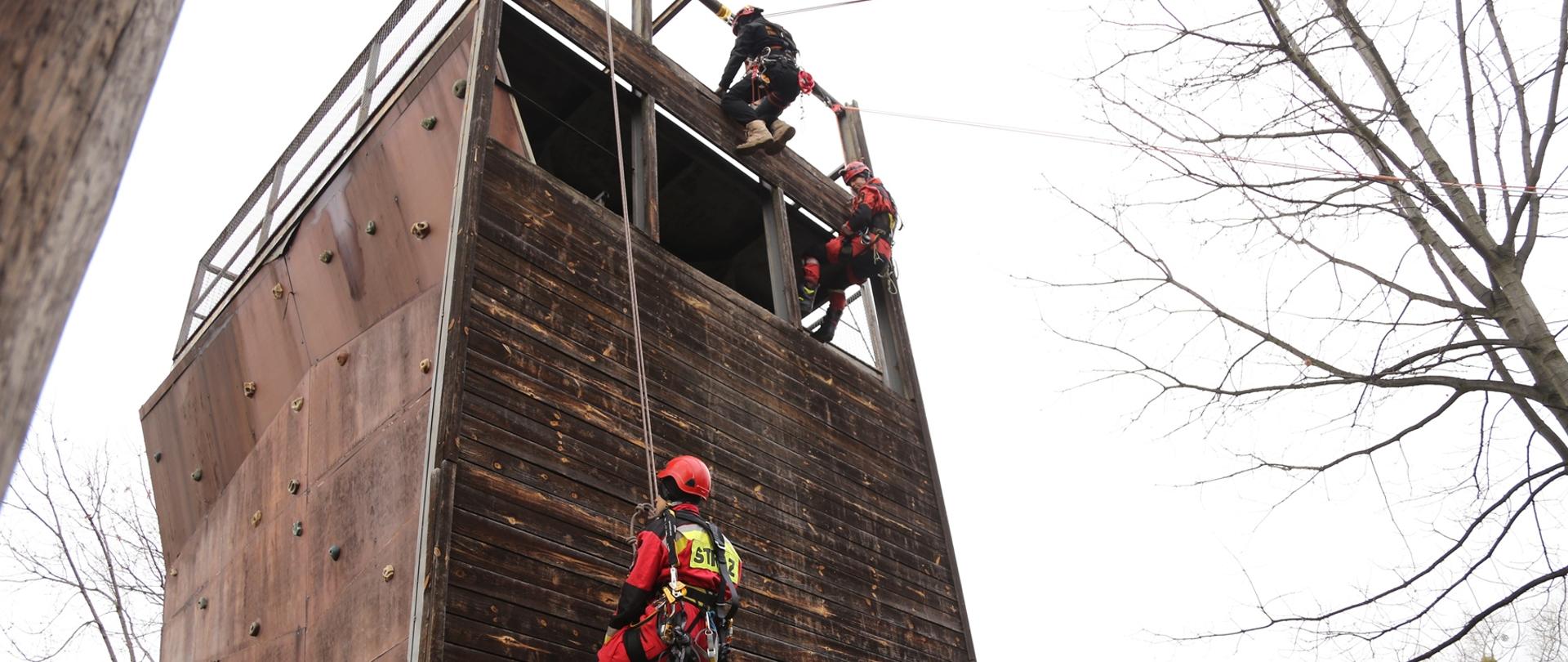 Troje ratowników wysokościowych zjeżdża na linach po ściance konstrukcji treningowej