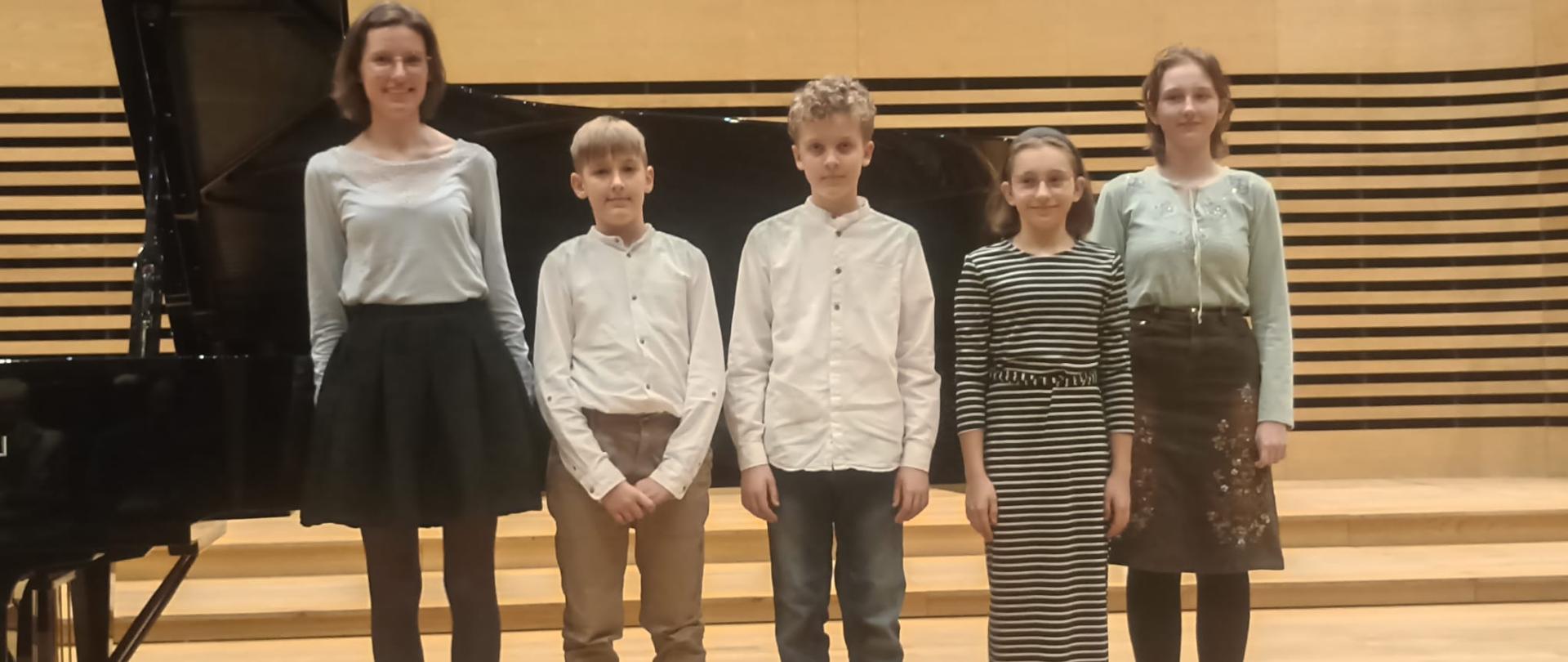 Uczniowie klasy Pani Edyty Suchanek z nauczycielem przy fortepianie na scenie sali koncertowej PSM, zbliżenie