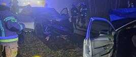 Uszkodzone dwa samochody osobowe po zderzeniu czołowym wokół strażacy