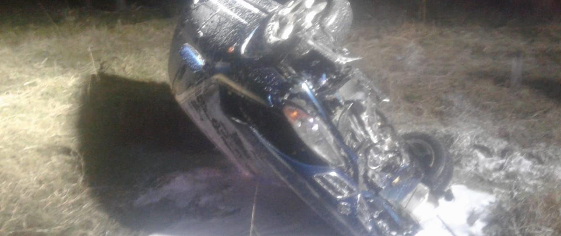 Samochód osobowy koloru niebieskiego znajduje się po za drogą wojewódzką numer dwieście osiemdziesiąt dziewięć. Wyniku dużej prędkości pojazd wypadł z pasa drogowego i dachował. Na poboczu leży samochód na boku od strony pasażera.